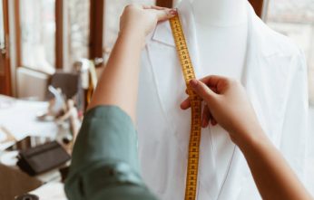 The main thing is right size. Woman designer is measuring white shirt with tape, close-up